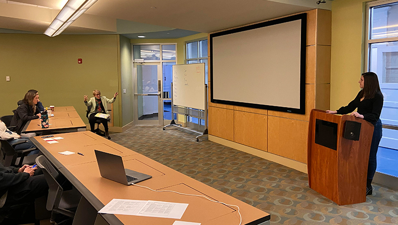 A student stands at a podium as a seated professor talks to them.