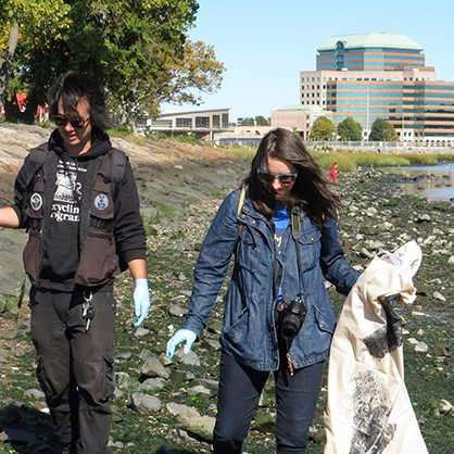 Two students walk the beach picking up trash.