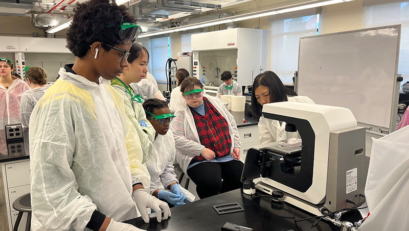 A group of students gathered at a microscope.