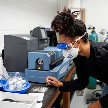 A student, wearing googles, examines minerals.