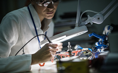 A women, in a lab coat, at a work table.